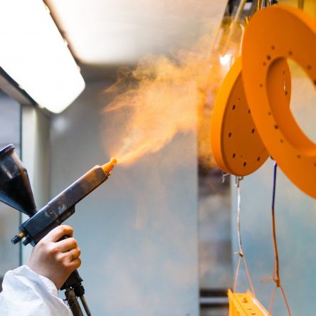 Powder coating of metal parts. A man in a protective suit sprays powder paint from a gun on metal products.